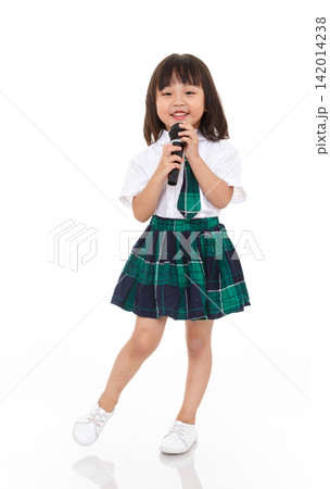 Happy and confident little school girl in uniform singing into a microphone, performing arts and childhood hobbies concept. Happy and confident little school girl in uniform singing into a microphone, performing arts and childhood hobbies concept. 142014238
