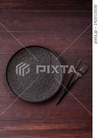 An empty round ceramic plate on a dark, textured brown background. An empty round plate An empty round ceramic plate on a dark, textured brown background. An empty round plate 142015030