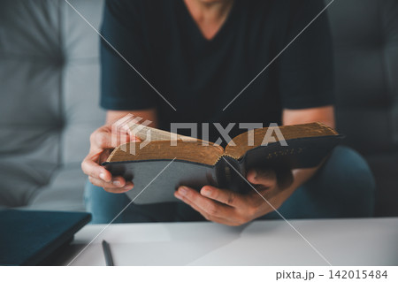 Close-up of an adult woman holding and reading an old Holy Bible at home, representing Christian faith, scripture study, devotion, spiritual guidance, wisdom, and hope. Close-up of an adult woman holding and reading an old Holy Bible at home, representing Christian faith, scripture study, devotion, spiritual guidance, wisdom, and hope. 142015484
