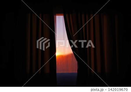 First rays of sunrise illuminating a window with flowing curtains in a tranquil setting 142019670