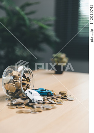 Coin jar spilling money with miniature cars on desk, symbolizing car savings, auto loan budget, vehicle purchase planning, transportation cost, and personal finance concept. 142019743