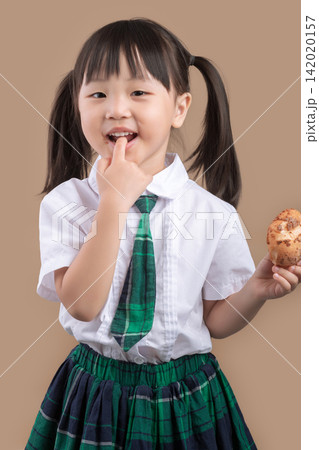 Hungry schoolgirl with pigtails taking a big bite of a delicious bread. Hungry schoolgirl with pigtails taking a big bite of a delicious bread. 142020157
