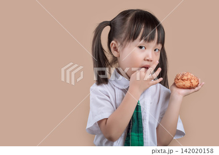 Hungry schoolgirl with pigtails taking a big bite of a delicious bread. Hungry schoolgirl with pigtails taking a big bite of a delicious bread. 142020158