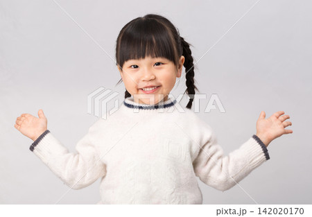 Cheerful little girl in white winter sweater spreading arms with an open friendly smile. Cheerful little girl in white winter sweater spreading arms with an open friendly smile. 142020170
