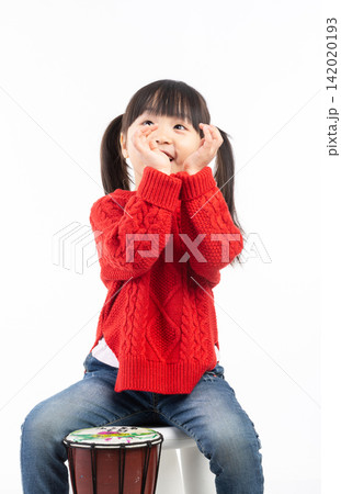 Smiling East Asian girl waving hand while playing an African djembe drum. Smiling East Asian girl waving hand while playing an African djembe drum. 142020193