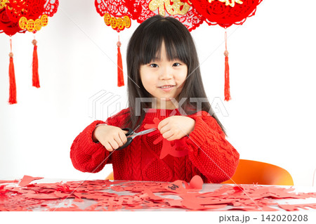 A little Asian girl wearing a bright red sweater is intently cutting red paper, preparing to welcome the Lunar New Year. 142020208