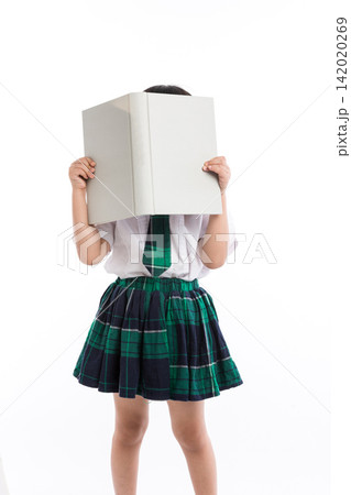Playful little student hiding her face behind a large open textbook in studio. Playful little student hiding her face behind a large open textbook in studio. 142020269