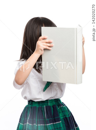 Playful little student hiding her face behind a large open textbook in studio. Playful little student hiding her face behind a large open textbook in studio. 142020270