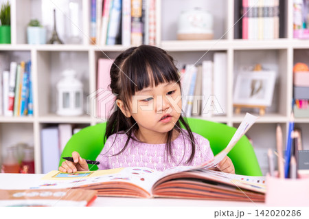 Attentive little student holding a pen and turning the page of a colorful textbook. Attentive little student holding a pen and turning the page of a colorful textbook. 142020286