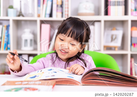 Attentive little student holding a pen and turning the page of a colorful textbook. Attentive little student holding a pen and turning the page of a colorful textbook. 142020287