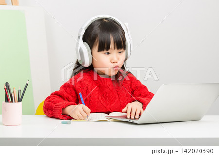 Attentive East Asian child using laptop and headphones for remote education at home. Attentive East Asian child using laptop and headphones for remote education at home. 142020390