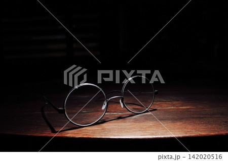 Giant round glasses resting on a small wooden table in soft lighting Giant round glasses resting on a small wooden table in soft lighting 142020516