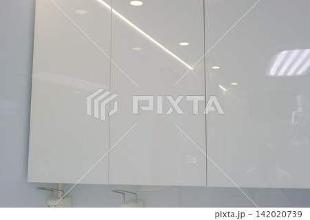 Modern white storage cabinet with three handleless doors in clean dental clinic or medical office creating minimalist healthcare interior close up professional furniture photography 142020739