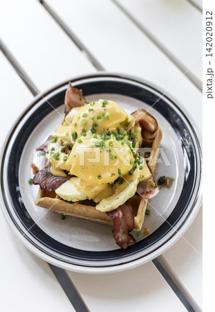 breakfast waffle with eggs hollandaise, bacon and avocado in modern garden cafe outdoor on sunny day breakfast waffle with eggs hollandaise, bacon and avocado in modern garden cafe outdoor on sunny day 142020912