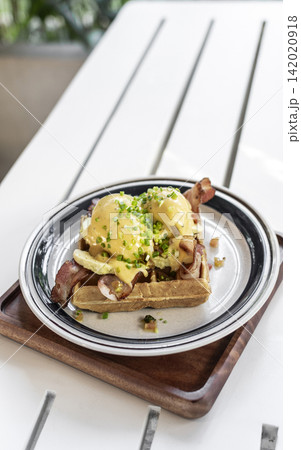 breakfast waffle with eggs hollandaise, bacon and avocado in modern garden cafe outdoor on sunny day 142020918
