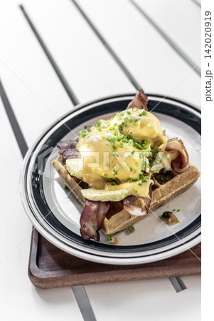 breakfast waffle with eggs hollandaise, bacon and avocado in modern garden cafe outdoor on sunny day breakfast waffle with eggs hollandaise, bacon and avocado in modern garden cafe outdoor on sunny day 142020919