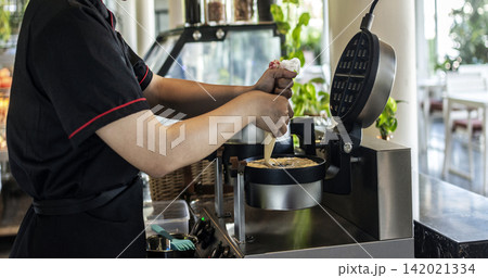 kitchen staff making fresh waffles in professional modern waffle cooking machine 142021334