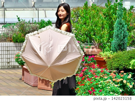 花壇のある明るい屋外テラスで日傘を手にする若い女性(夏・紫外線対策) 花壇のある明るい屋外テラスで日傘を手にする若い女性(夏・紫外線対策) 142023158