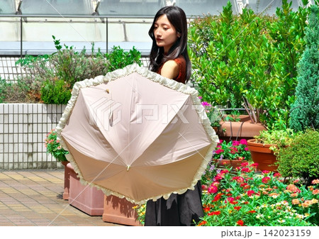 花壇のある明るい屋外テラスで日傘を手にする若い女性(夏・紫外線対策) 花壇のある明るい屋外テラスで日傘を手にする若い女性(夏・紫外線対策) 142023159