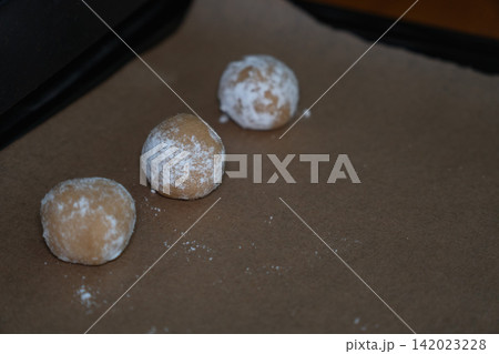 Raw almond cookie dough balls coated with powdered sugar rest on baking paper before baking. Home baking, dessert preparation, handmade pastry, confectionery, recipe, baking process Raw almond cookie dough balls coated with powdered sugar rest on baking paper before baking. Home baking, dessert preparation, handmade pastry, confectionery, recipe, baking process 142023228