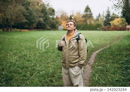 Happy 30s blonde man with backpack standing in the countryside. Traveler. Autumn time. Positive handsome blonde male standing outdoor 142023284
