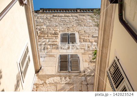 A narrow alleyway between historic stone buildings with weathered facades and wooden shutters A narrow alleyway between historic stone buildings with weathered facades and wooden shutters 142023524