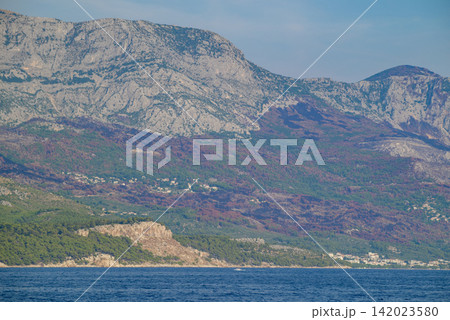 A panoramic view of a rugged coastal landscape with a massive rocky mountain range rising sharply from the sea A panoramic view of a rugged coastal landscape with a massive rocky mountain range rising sharply from the sea 142023580