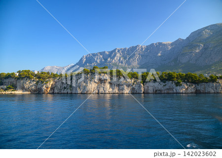 A dramatic coastal landscape with a rugged white limestone cliff stretching horizontally across the frame A dramatic coastal landscape with a rugged white limestone cliff stretching horizontally across the frame 142023602