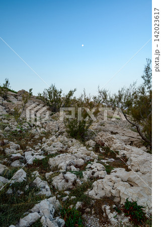 A rugged, rocky landscape under a clear sky with sparse vegetation and a soft blue sky gradient A rugged, rocky landscape under a clear sky with sparse vegetation and a soft blue sky gradient 142023617