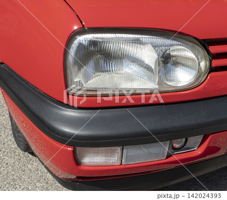 Tavernes Blanques, Spain - June 14, 2026. Close up of the headlight assembly and bumper of a red Volkswagen Golf at a parking lot during daytime Tavernes Blanques, Spain - June 14, 2026. Close up of the headlight assembly and bumper of a red Volkswagen Golf at a parking lot during daytime 142024393