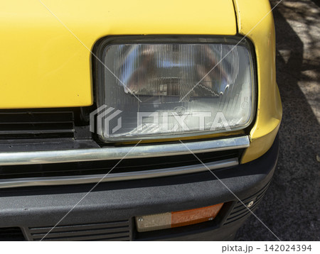 Tavernes Blanques, Spain - June 14, 2026. Close up of the front headlight assembly and bumper trim of a yellow Renault TL taken in a sunny outdoor setting Tavernes Blanques, Spain - June 14, 2026. Close up of the front headlight assembly and bumper trim of a yellow Renault TL taken in a sunny outdoor setting 142024394