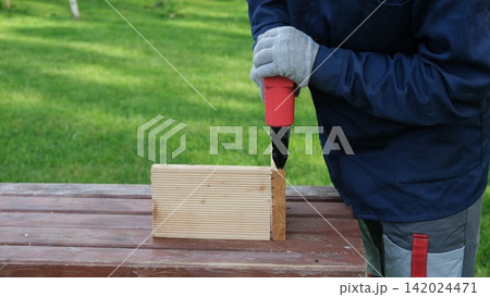 Cropped Image of Male Carpenter shooting nails on wooden frame outdoor. Industrial Cordless Nail Gun Power Tool. Tools efficient for framing, electrical. Carpenter using Air Nailer on timber. Woodwork 142024471
