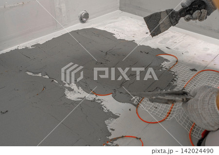 Electric Heating Mat Installing in the Tile Adhesive. Underfloor Dual Core Fiberglass Mesh Mat. Warm Floor Heating System. Warming. Worker Applying Concrete Mortar for Warm Floor. Renovation work. 4K Electric Heating Mat Installing in the Tile Adhesive. Underfloor Dual Core Fiberglass Mesh Mat. Warm Floor Heating System. Warming. Worker Applying Concrete Mortar for Warm Floor. Renovation work. 4K 142024490