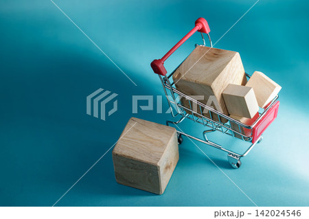 Close up of a mini metal shopping cart packed with blank wooden blocks next to a cube against a vibrant turquoise background. High Quality Photo Close up of a mini metal shopping cart packed with blank wooden blocks next to a cube against a vibrant turquoise background. High Quality Photo 142024546
