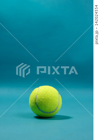 Single bright yellow tennis ball resting on a solid blue surface with copy space above. High Quality Photo 142024554