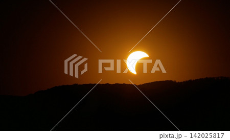 Partial solar eclipse above mountain silhouette - glowing crescent sun, astronomy, nature and cosmic phenomenon concept. 142025817