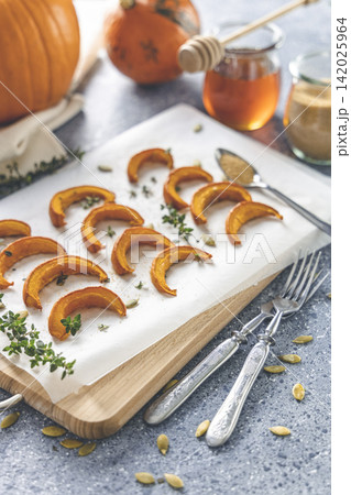 Baked mini pumpkin slices with thyme on a wooden board over grey table. Seasonal food vegetarian recipe. Baked mini pumpkin slices with thyme on a wooden board over grey table. Seasonal food vegetarian recipe. 142025964
