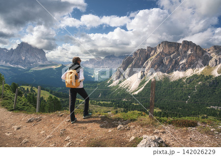 Woman with yellow backpack standing on trail looking at mountain Woman with yellow backpack standing on trail looking at mountain 142026229
