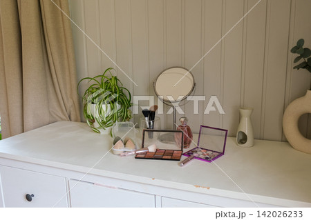 Vanity round mirror and make up items arranged on desk under lamp, palettes and brushes, open eyeshadow, cotton pads. Makeup and self care at home concept. Personal beauty products items on table. 142026233