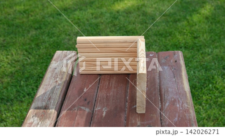 Wooden billet bar for work on table in the green grass summer backyard. Wood board plank on outdoor workshop surface. Home DIY. No people. Woodworking, timber. Building a garden bed, hive, furniture Wooden billet bar for work on table in the green grass summer backyard. Wood board plank on outdoor workshop surface. Home DIY. No people. Woodworking, timber. Building a garden bed, hive, furniture 142026271