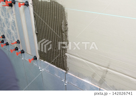 Worker Laying Ceramic Tiles on the Wall. Repairman Placing White Gray Square Tiles, Applying Adhesive. Builder Installing Tile Using Leveler, Tile Leveling Clips. Tiling. Finishing Repair Work. 4K Worker Laying Ceramic Tiles on the Wall. Repairman Placing White Gray Square Tiles, Applying Adhesive. Builder Installing Tile Using Leveler, Tile Leveling Clips. Tiling. Finishing Repair Work. 4K 142026741