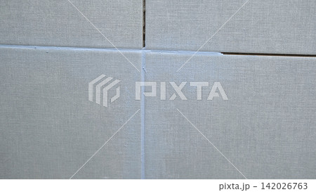 Worker using a rubber grout float to smooth grout between tiles. Carefully applying sealant to tiles joints. Workman hands smoothing caulk, using small tool to remove excess and create clean seam. 142026763