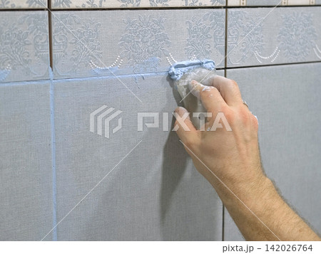 Worker using a rubber grout float to smooth grout between tiles. Carefully applying sealant to tiles joints. Workman hands smoothing caulk, using small tool to remove excess and create clean seam. Worker using a rubber grout float to smooth grout between tiles. Carefully applying sealant to tiles joints. Workman hands smoothing caulk, using small tool to remove excess and create clean seam. 142026764