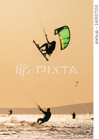 Kite boarder performing a high jump over the sea against a warm sunset Kite boarder performing a high jump over the sea against a warm sunset 142027333
