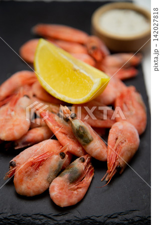 A close-up of frozen pink shrimp with eyes, a bright slice of lemon on top of a handful, the background is blurred. Concept: highlighting seafood details and citrus accents, macro photography. High A close-up of frozen pink shrimp with eyes, a bright slice of lemon on top of a handful, the background is blurred. Concept: highlighting seafood details and citrus accents, macro photography. High 142027818