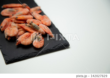 Frozen pink shrimps with a clear touch of frost and a cold sheen are laid out on a black slate board on a white background. The concept: a concise presentation of a frozen product. High quality photo Frozen pink shrimps with a clear touch of frost and a cold sheen are laid out on a black slate board on a white background. The concept: a concise presentation of a frozen product. High quality photo 142027829