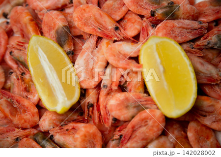 A close-up of a filled frame with tightly lying frozen pink shrimp and two bright lemon slices creating a contrast. Concept: filling the space with seafood texture. High quality photo 142028002