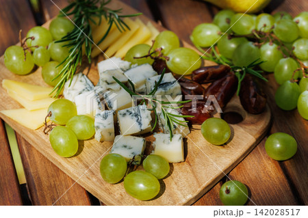 Cheese platter with grapes and rosemary on wooden board Cheese platter with grapes and rosemary on wooden board 142028517