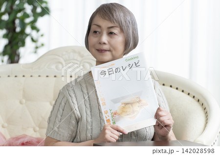 リビングのソファーで料理雑誌を見るシニア女性 142028598