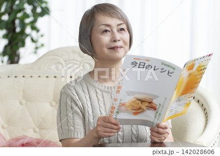 リビングのソファーで料理雑誌を見るシニア女性 142028606